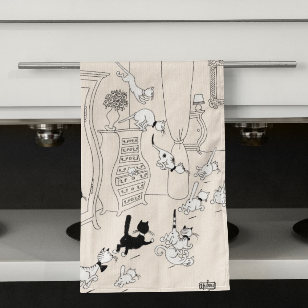 Tea towel with black and white cat illustration hanging on a kitchen cabinet.