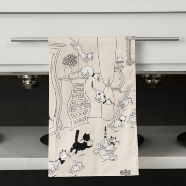 Tea towel with black and white cat illustration hanging on a kitchen cabinet.