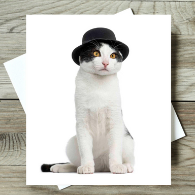 Cat wearing a black top hat on a white card with envelope, on a wooden surface