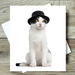 Cat wearing a black top hat on a white card with envelope, on a wooden surface