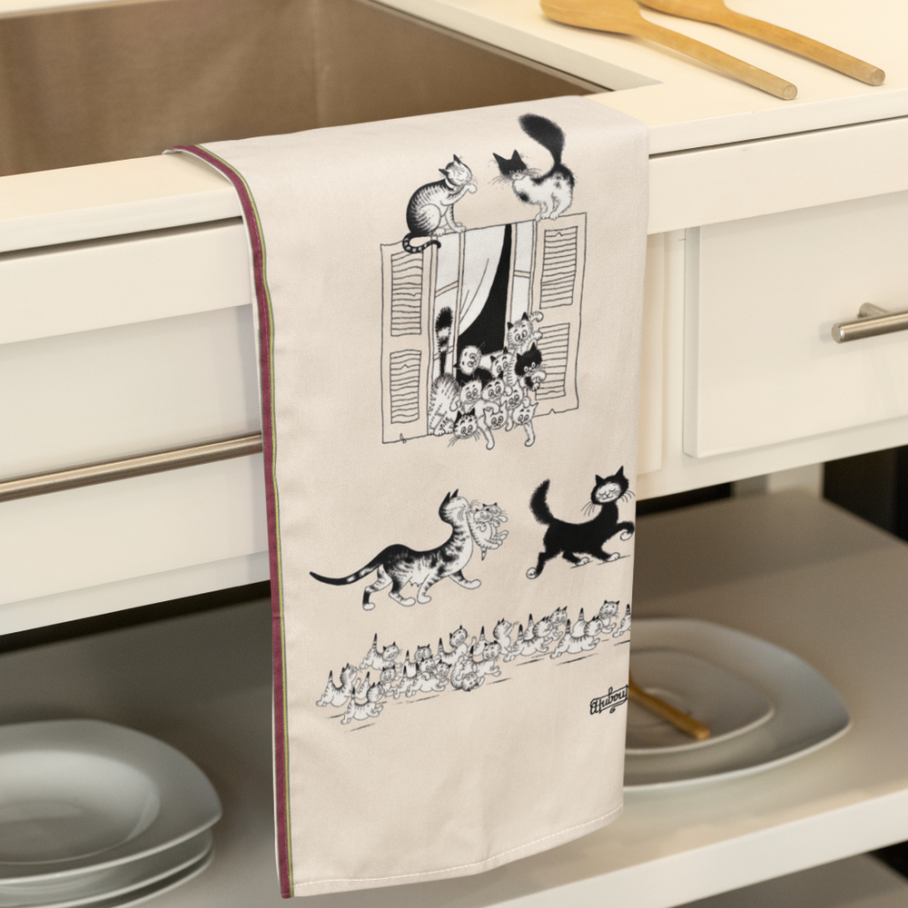 Kitchen towel with cat illustrations hanging on a kitchen cabinet.