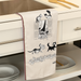 Kitchen towel with cat illustrations hanging on a kitchen cabinet.