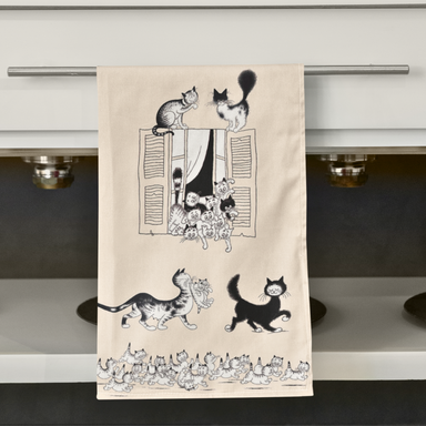 Beige towel with black and white cat illustrations hanging on a kitchen rack.