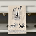 Beige towel with black and white cat illustrations hanging on a kitchen rack.