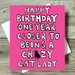 Pink birthday card with text 'Happy Birthday one year closer to being a crazy cat lady' on a wooden surface.