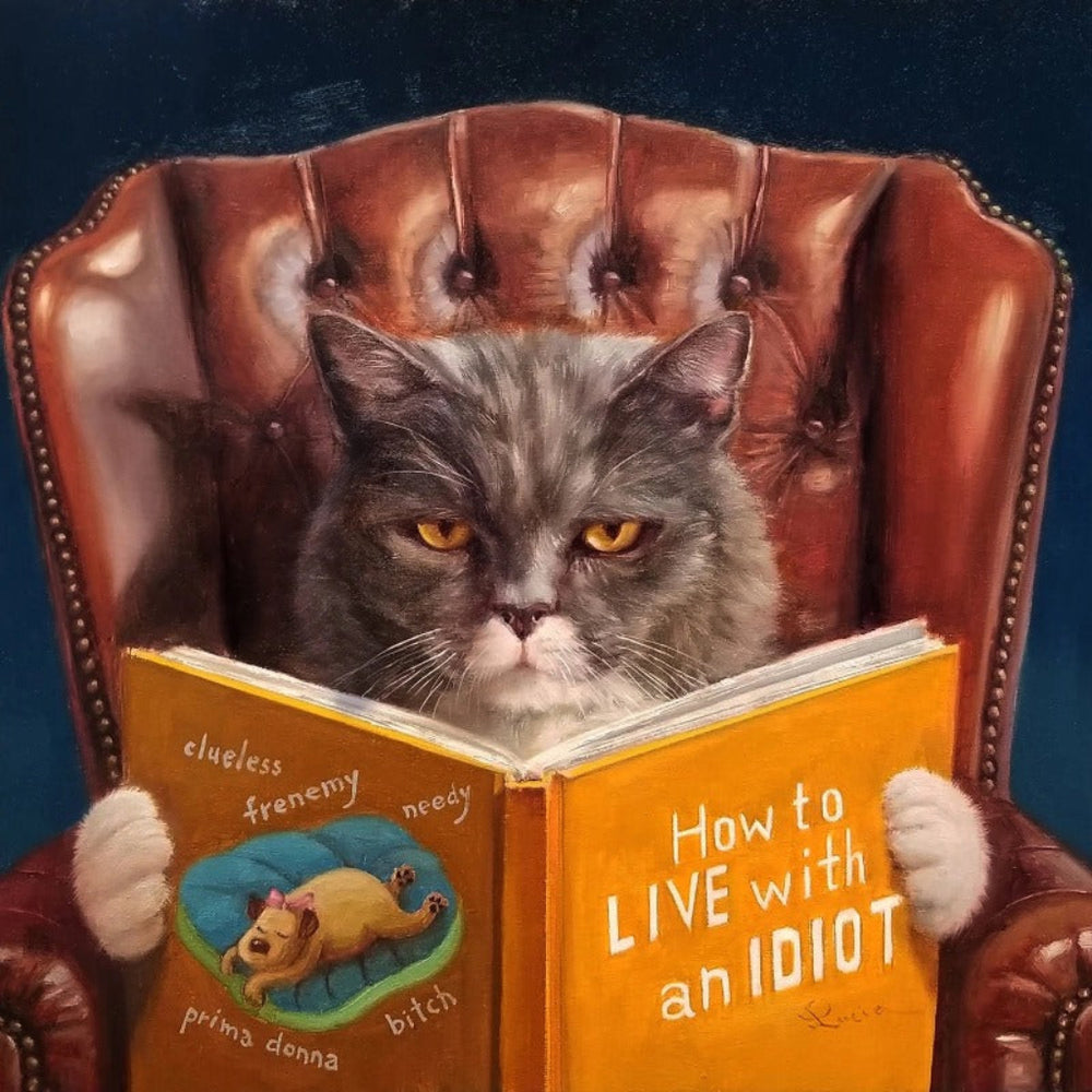 Cat sitting in a leather armchair reading a book titled 'How to Live with an Idiot'.