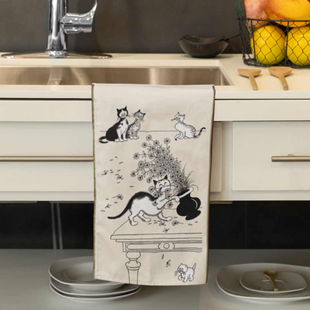 Kitchen towel with cat illustrations hanging on a kitchen counter.