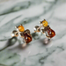 A pair of sterling silver cat-shaped earrings with amber gemstones set in them, displayed on a marble surface.