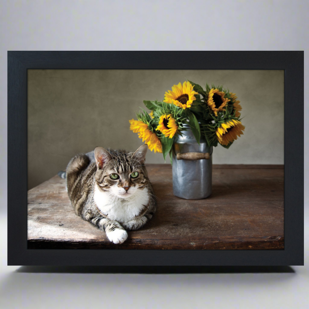 A lap tray with a printed image of a cat lying next to a vase of sunflowers on a wooden table.