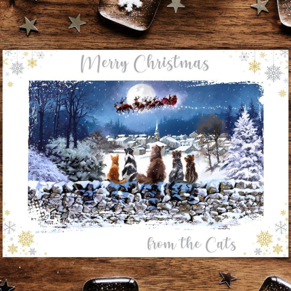 A Christmas greeting card featuring a painting of five cats on a drystone wall with Santa's sleigh in the background, set against a snowy landscape.
